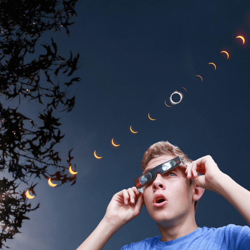Person with eclipse glasses looking up at the stages of a solar eclipse in a darkening sky, with tree silhouettes on the side